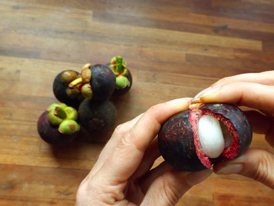 Open the mangosteen by pulling the top of and gently squeezing until it cracks down the center.